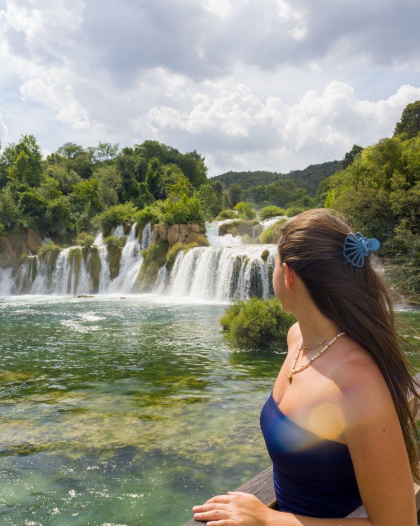 Woman standing on a wooden viewpoint looking at Skradinski Buk waterfalls in Krka National Park, Croatia.