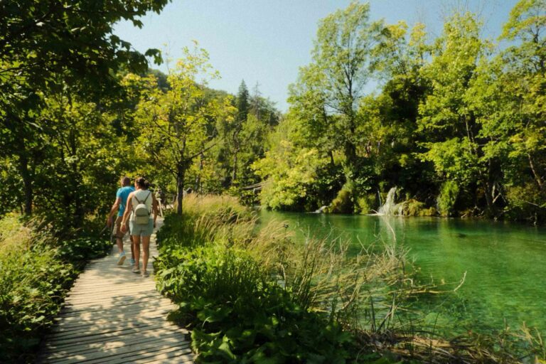 People walking along the wooden boardwalk beside emerald-green water at Plitvice Lakes National Park, Croatia.
