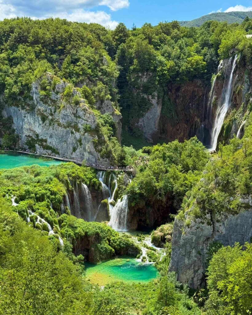 Turquoise lakes, cascading waterfalls, and wooden boardwalk at Plitvice Lakes National Park in Croatia surrounded by lush forest and cliffs.